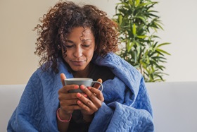 Sick woman wrapped in blanket holding a mug