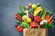 Fruits and vegetables spilling out of a paper shopping bag onto a slate background