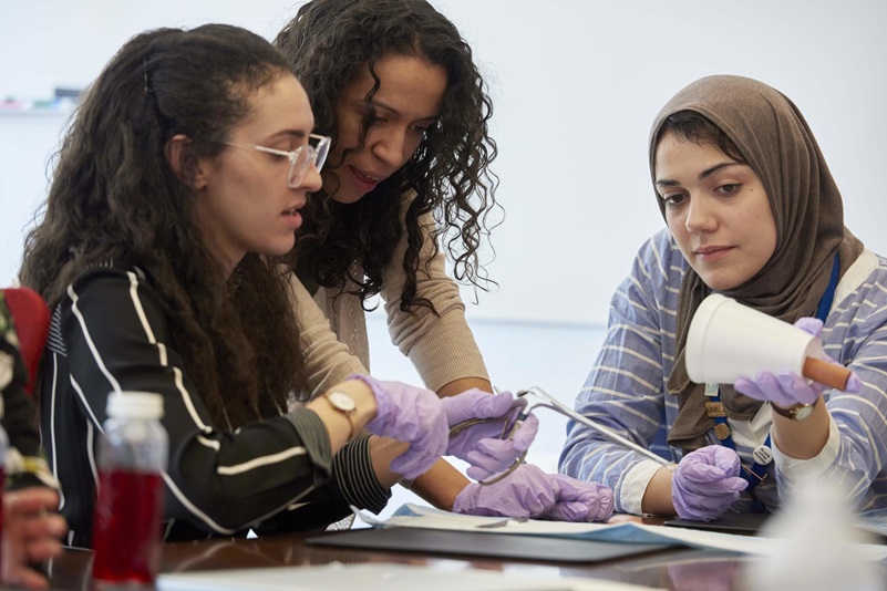 Three women at a table examining medical instruments.