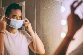 Man putting on a face mask while looking in the mirror