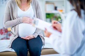 Pregnant woman holding her stomach while talking to a doctor in the hospital