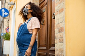 Pregnant woman wearing overalls and a facemask outdoors
