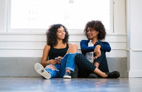 Two women wearing jeans and sitting on the floor having a conversation