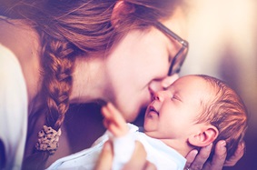 young_mom_wearing_glasses_with_braided_hair_kisses_new_born_baby