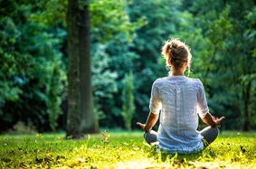Woman sitting on the ground meditating surrounded by trees