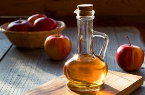 A small bottle of apple cider vinegar surrounded by apples