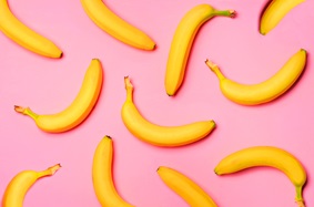 11 unpeeled loose bananas arranged on a pink background