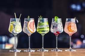 Five clear drinks and fruit in wine glasses on a bar