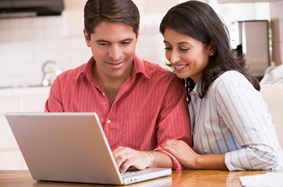 a couple sitting at a counter and looking at a laptop