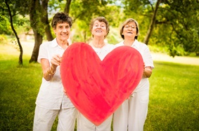 Three older women holding a giant red heart.