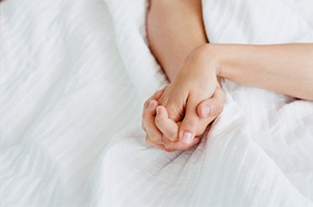 a couple's hands holding each other in bed