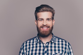 a man with a beard smiling and wearing a plaid shirt
