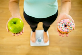 Woman standing on scale holding an apple and a doughnut