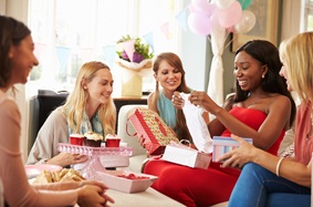 a group of women watching one woman open presents at a baby shower
