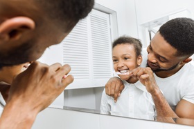 A father helps his daughter brush her teeth