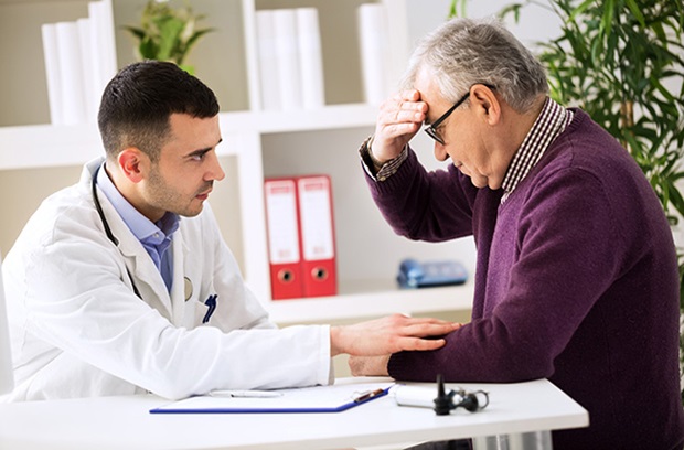 man holding head while sitting across from male doctor