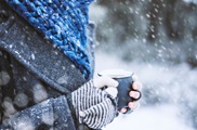 Person wearing gloves and a scarf, holding a mug, in the snow