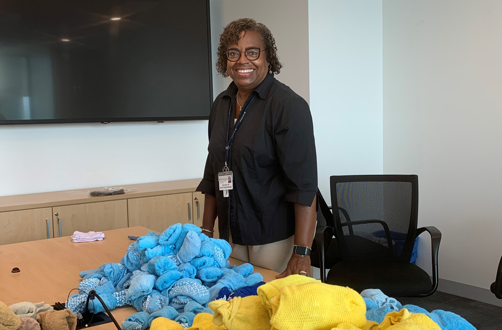 Poppy Bass, senior project manager in Information Services, stands smiling behind a table covered with piles of socks