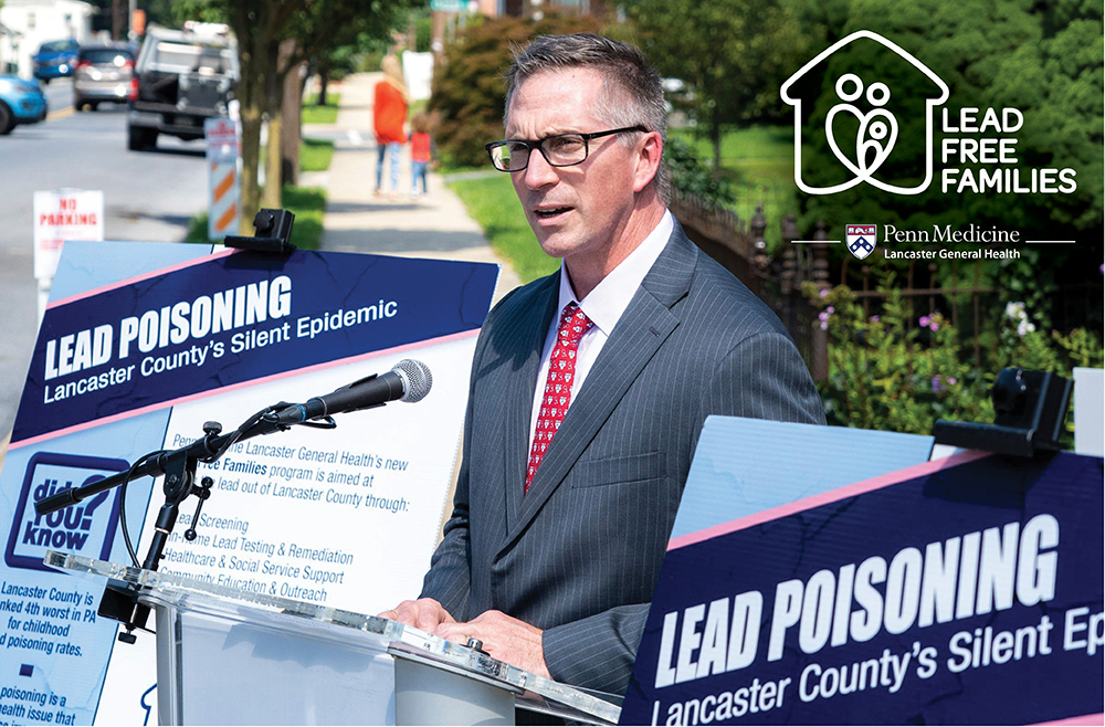 John J. Herman, CEO of Penn Medicine Lancaster General Health, speaks at outdoor podium surrounded by signs about lead poisoning in Lancaster County.