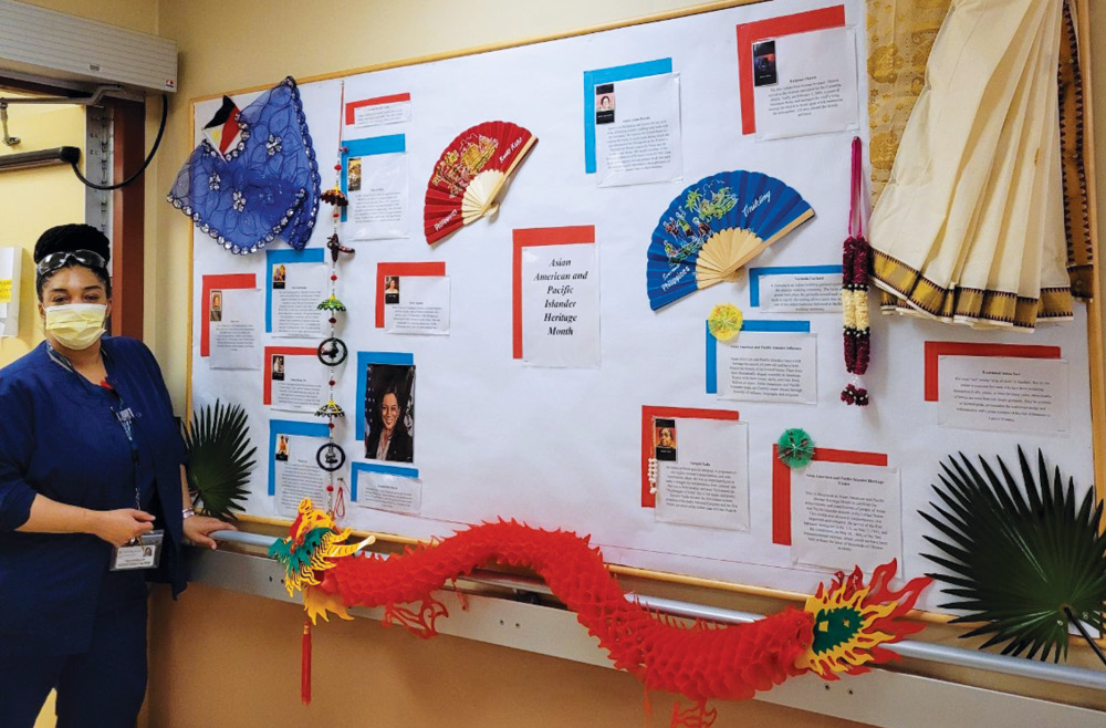 Fayonna Gray, RN stands with the AAPI Heritage Month Bulletin Board She Created for the Month of May