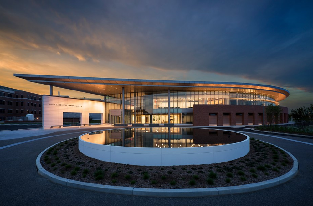Photo of ABBCI in the evening. The sun sets behind the glass building. There is also a fountain in front of the building.