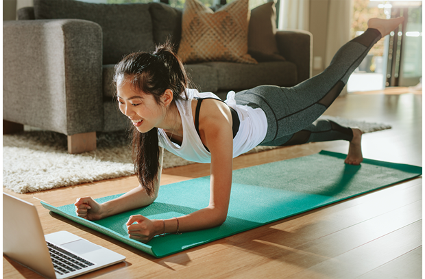 A woman working out in her home in front of a laptop.