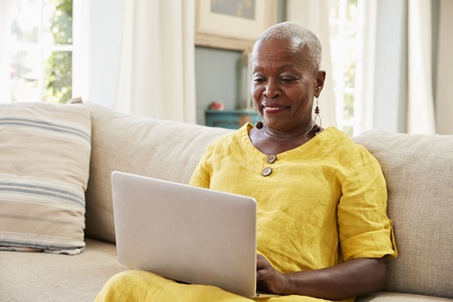 Mature woman sitting on a couch while using a laptop.